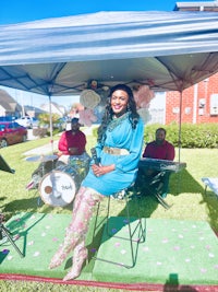a woman in a blue dress sitting on a chair under a tent
