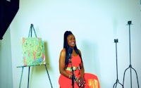 a woman in an orange dress sitting in front of an easel